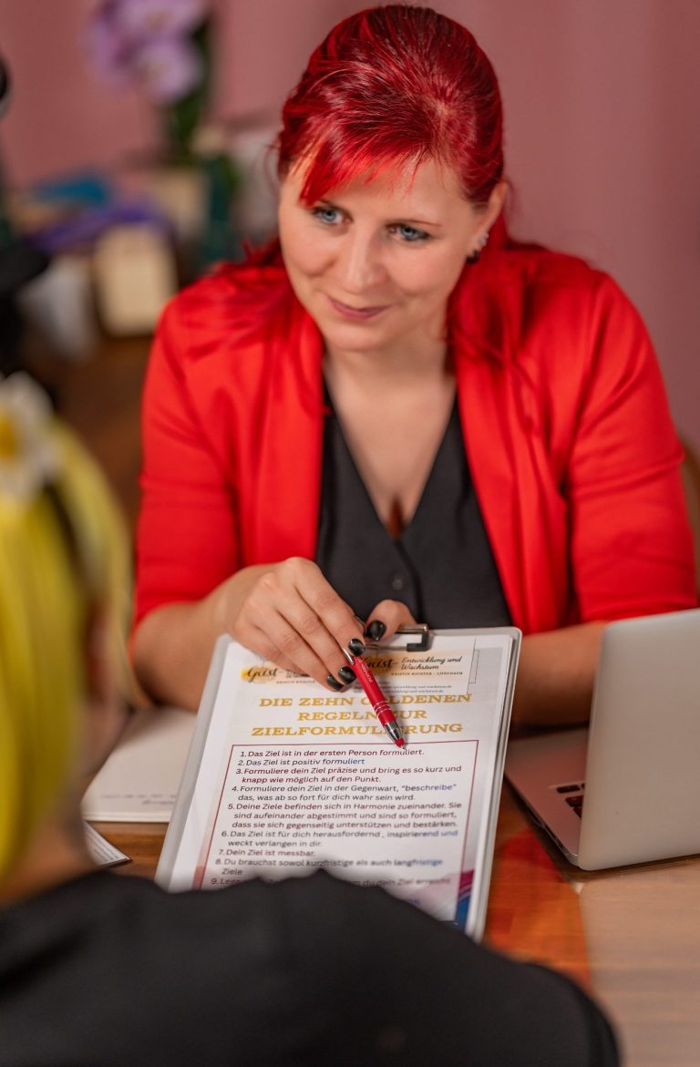 Deine Transformation Eine Person mit rotem Blazer hält ein Notizbuch und einen Stift in der Hand.