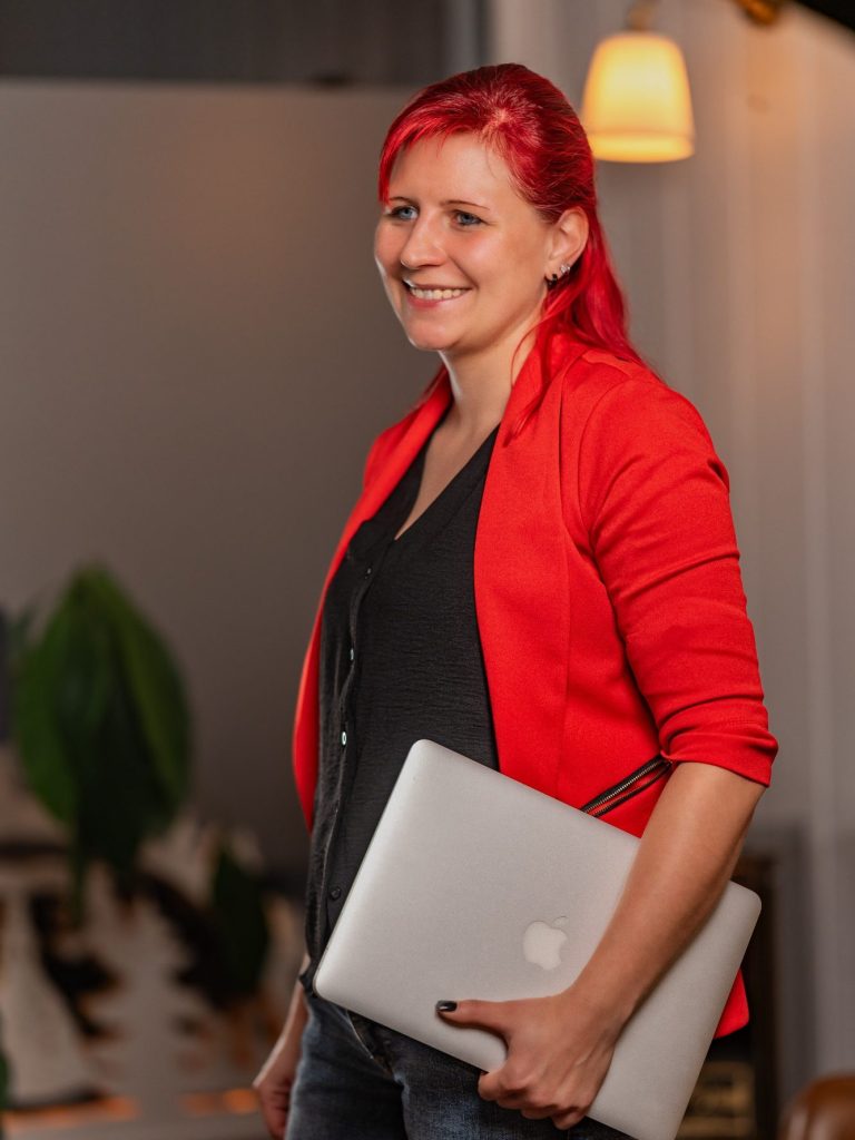 Buche deine Transformation Frau mit rotem Blazer und schwarzem Oberteil, die am Telefon lächelt.